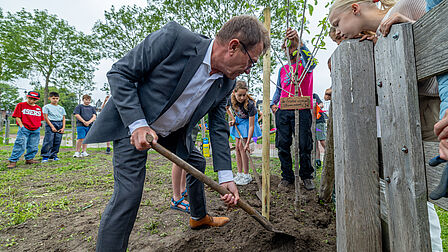 Wethouder Does plantte een kersenboom om het tienjarig bestaan van de schooltuin bij IKC de Helix te vieren.