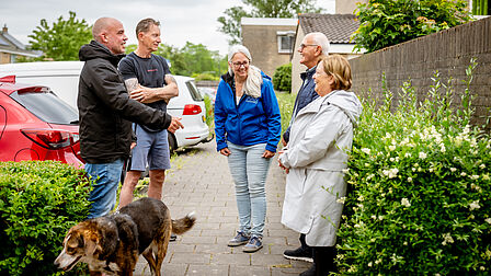 Vier mensen staan buiten op de stoep. Van deze vier mensen is één mevrouw Rachel. 