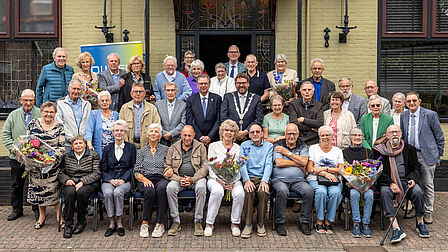Alle jubilerende echtparen poseren met elkaar voor d eentree van restaurant de Burg. In hun midden de burgemeester en wethouder Rep.