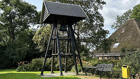 Afbeelding van een historische luidklok. Een bel op palen onder een dakje.