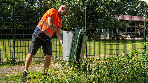 afbeelding van een mederwerker van de gemeente die een openbare afvalbak leegt.