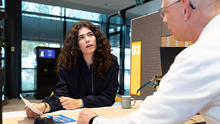 mevrouw zit aan de balie in het gemeentehuis en praat met medewerker