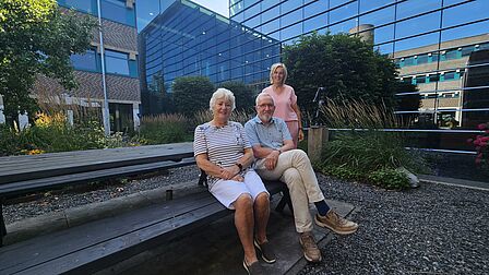 Drie mensen zitten op een picknicktafel en lachen richting de camera.. 