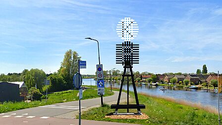 Baken met de K en P erop tussen het groen, de weg en het water.