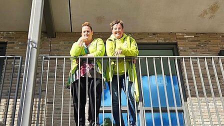 Twee vrouwen poseren op de galerij van een appartementencomplex