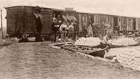Een oude foto van een mensen in een trein bij bootjes vol met witte kool.